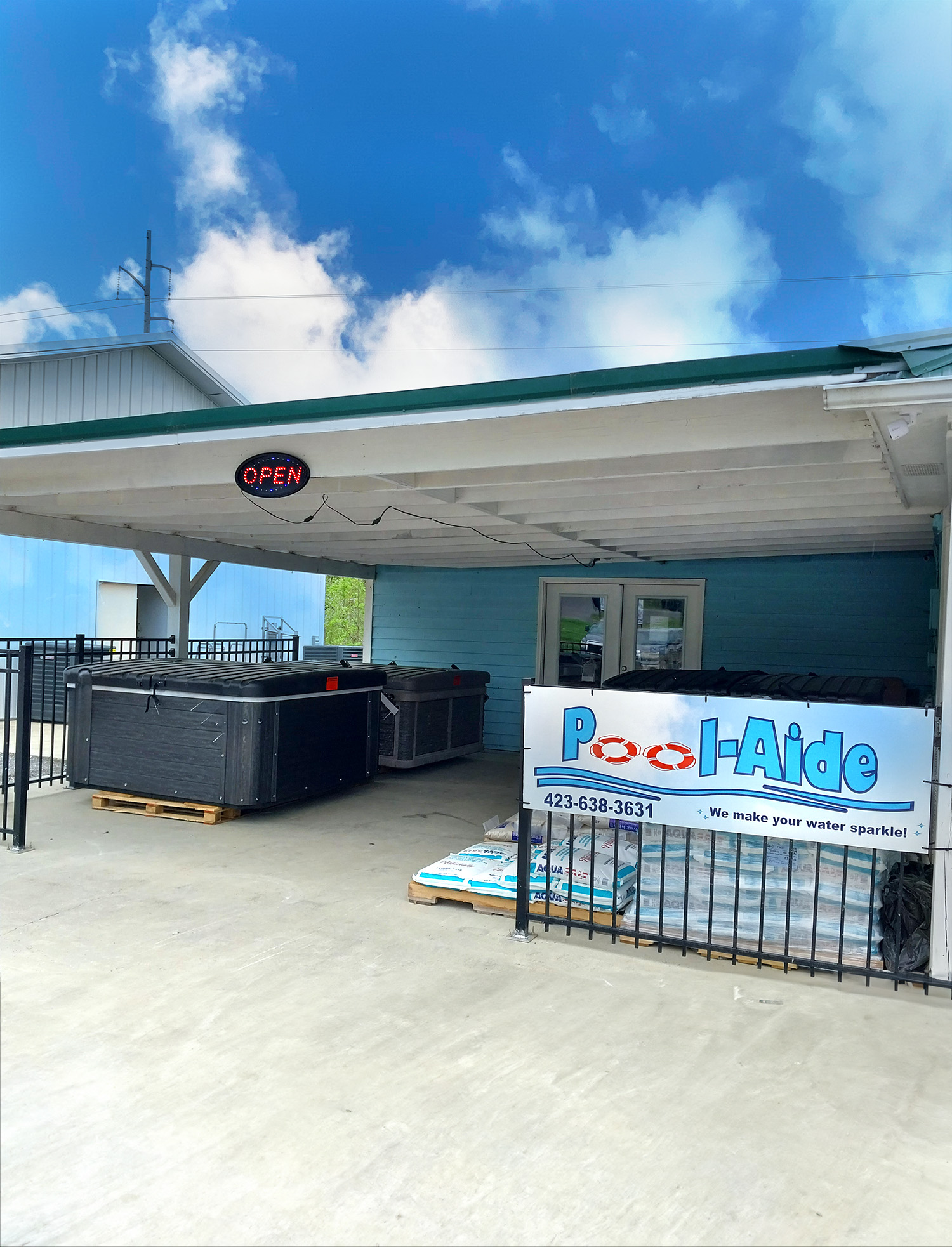 Exterior view of the Pool-Aide storefront including signage, spas, and pallets with bags of sand and pool chemicals